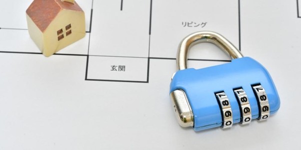 住宅模型とダイヤル式南京錠が置かれた住宅の間取り図。防犯対策や不動産セキュリティを示唆するイメージ