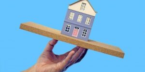 傾いた家の模型を手のひらに乗せたイメージ(地震による住宅の不安定さの表現)