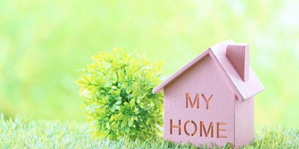 芝生の上に「MY HOME」と書かれた木の家のオブジェと植物が置かれている、明るく爽やかなイメージの写真