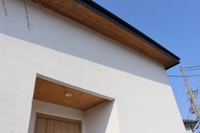 白い外壁と木目の軒天が特徴的な住宅の玄関まわり