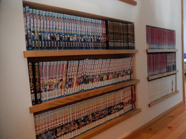 壁面に設けられた木製の棚に並ぶ大量の漫画本コレクション
